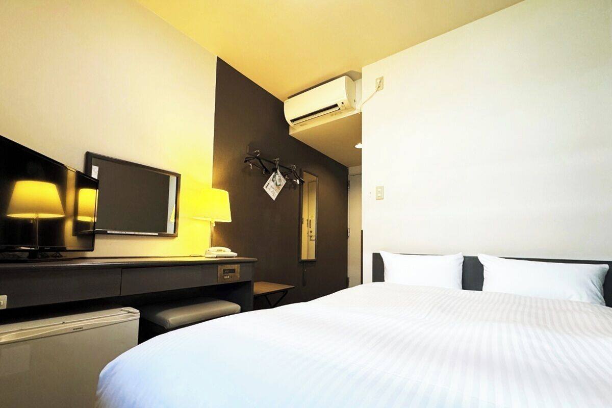 Hotellihuone, jossa on suuri sänky, työpöytä lampun kanssa, televisio ja ilmastointilaite.