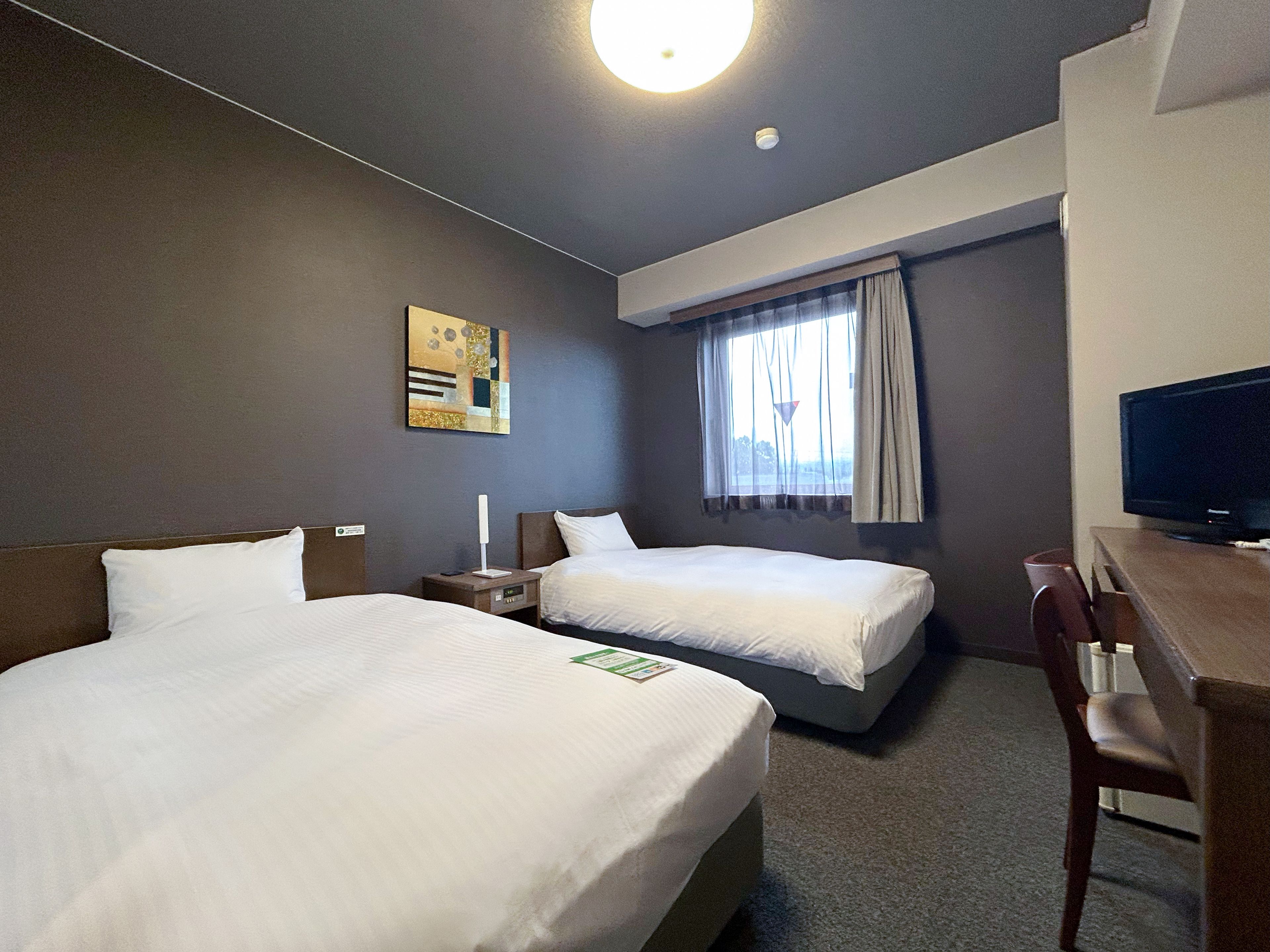 A hotel room with two beds, a desk, a television, and a window with curtains.