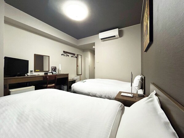 Een hotelkamer met twee bedden, een bureau met een computer, een televisie en een airconditioning.