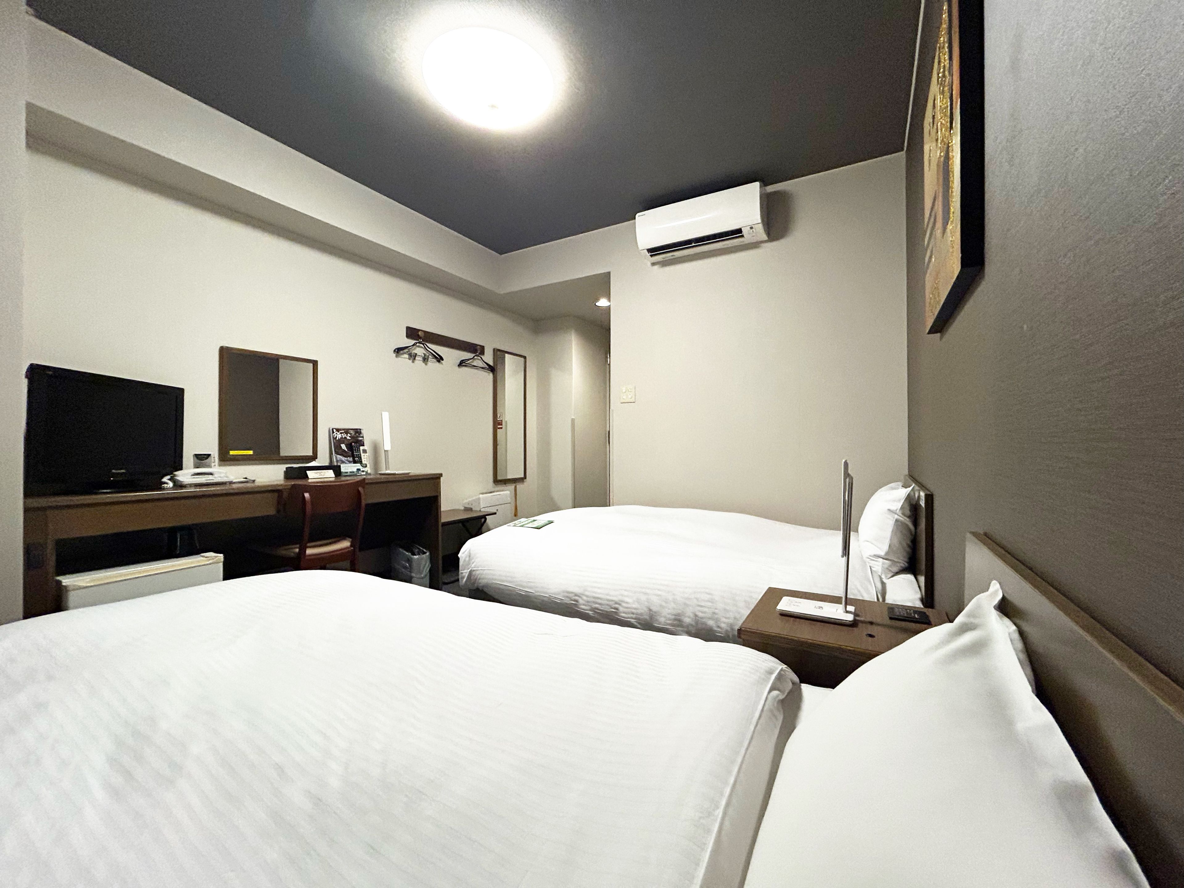 Habitación de hotel con dos camas, un escritorio con ordenador, televisor y aire acondicionado.