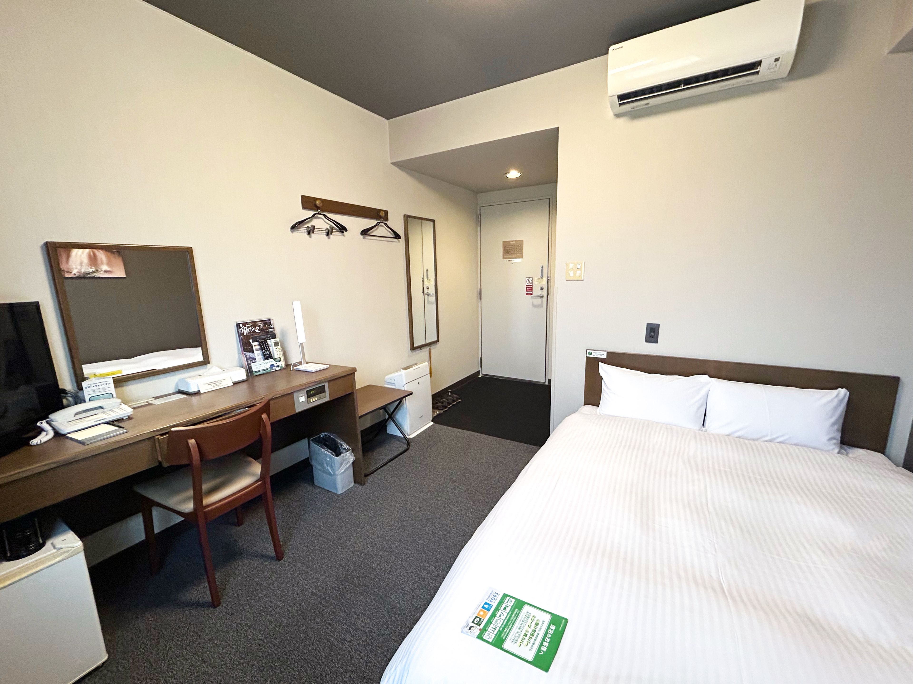 A hotel room with a bed, desk, chair, and an air conditioning unit.