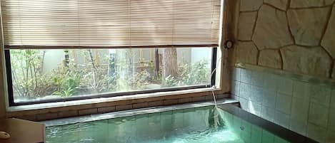 A room with a glass-enclosed hot tub, a window with blinds, and a stone wall.
