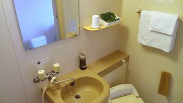 A bathroom with a sink, toilet, and a mirror. There is a shelf with a tissue box and a bottle of hand soap.