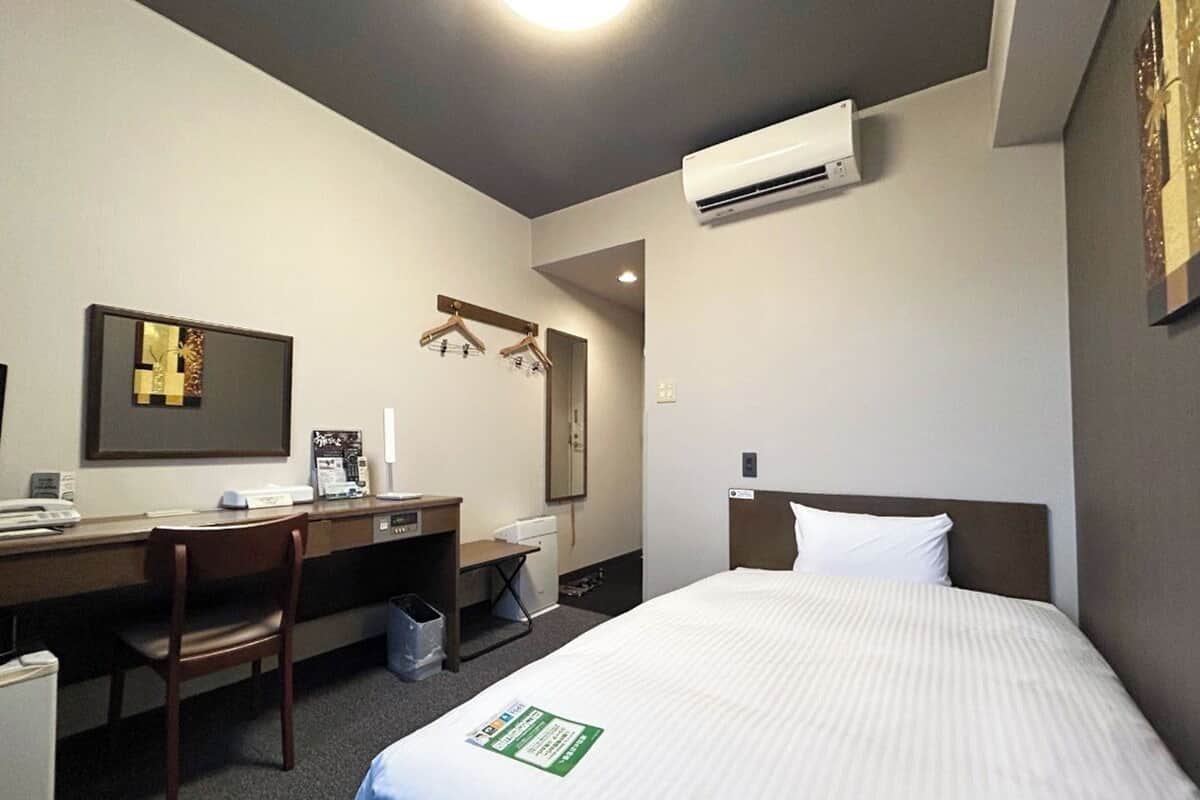Ein Hotelzimmer mit Bett, Schreibtisch, Stuhl, Mülleimer und Klimaanlage.