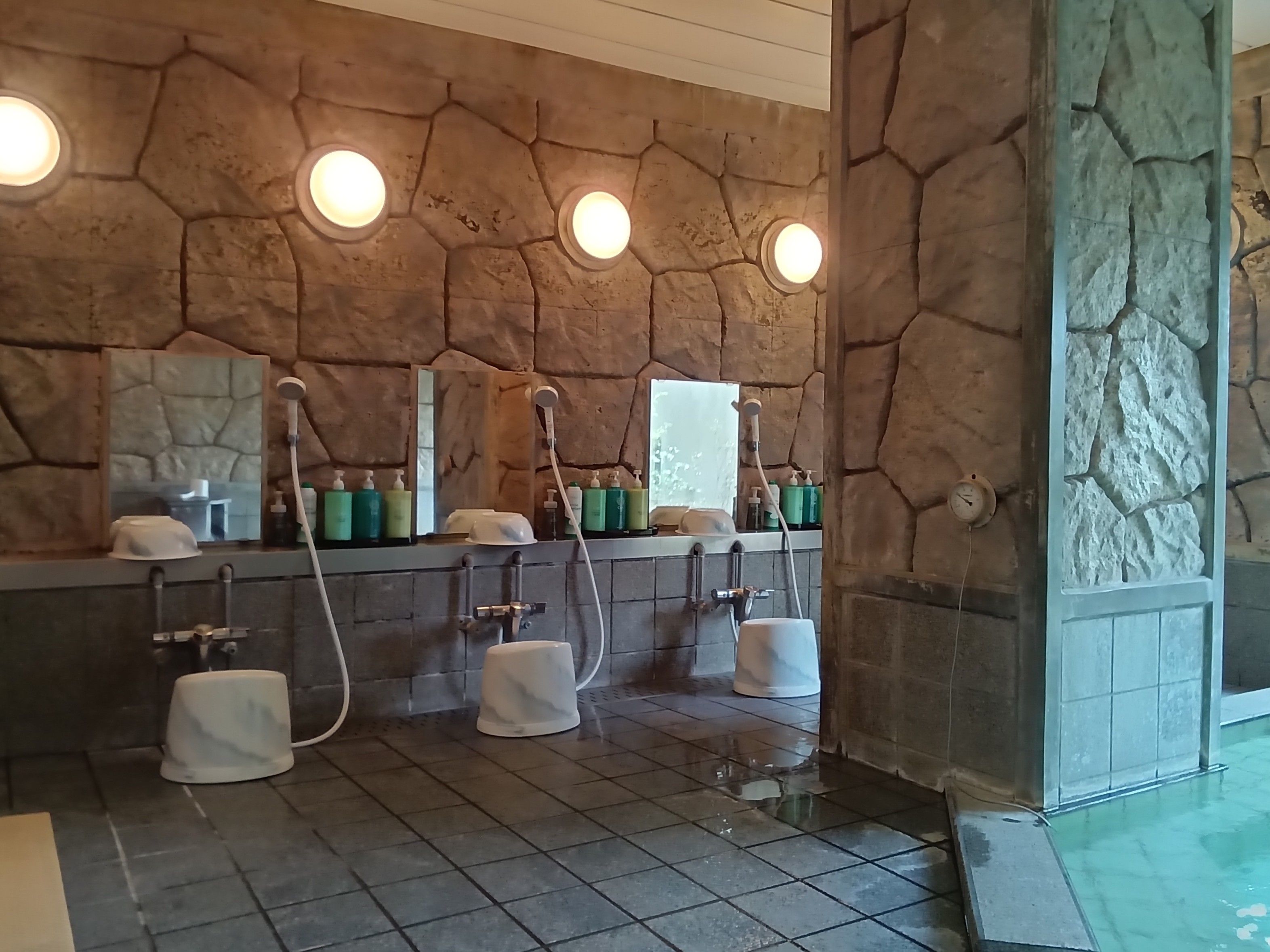 A bathroom with a stone wall, multiple sinks, and a mirror.
