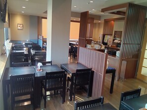 A restaurant with multiple tables and chairs, a counter with various items, and a partition with vertical slats. - Hotel Route Inn Myoko Arai (Myoko)