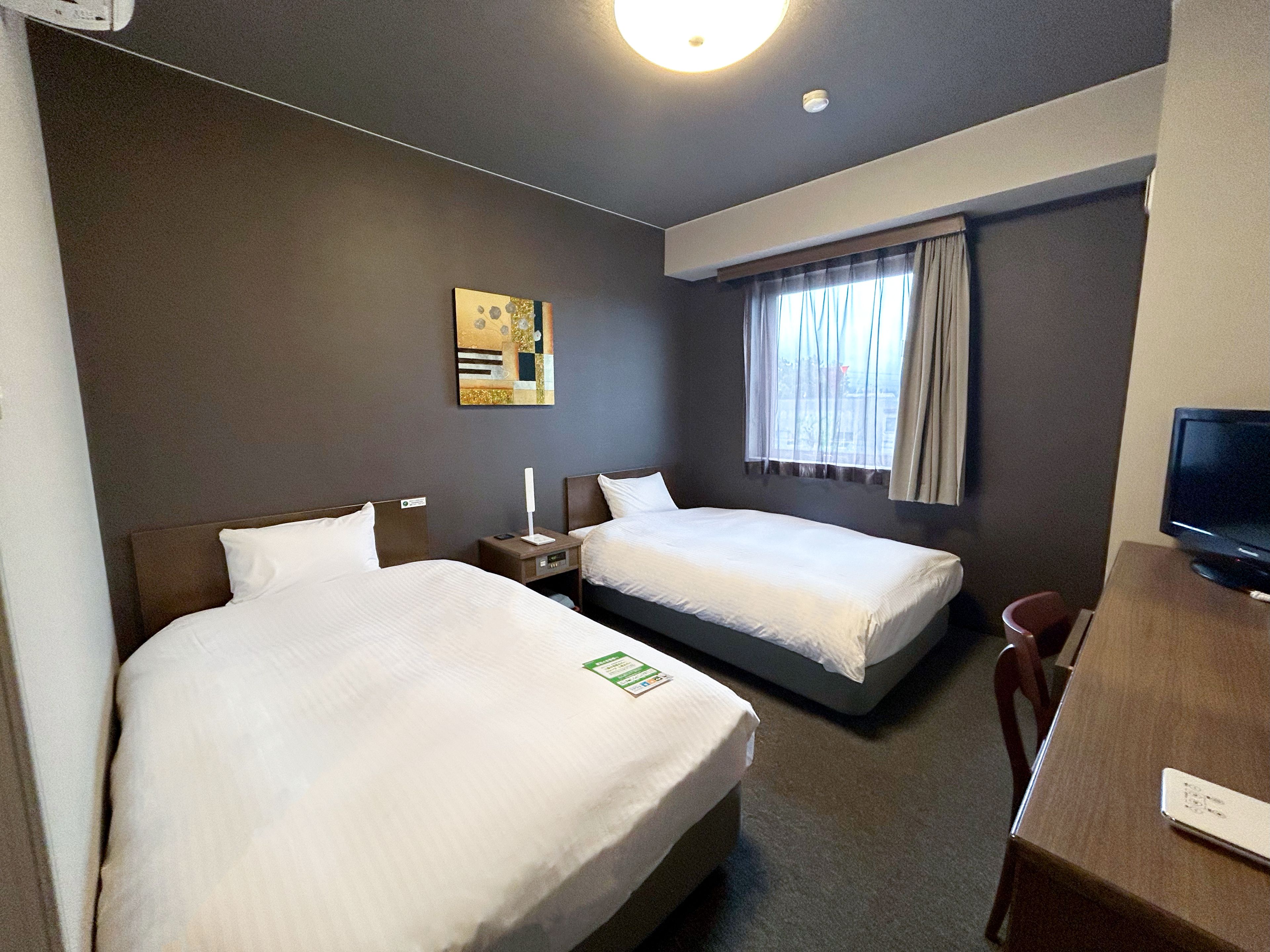 A hotel room with two beds, a desk, a television, and a window with curtains.