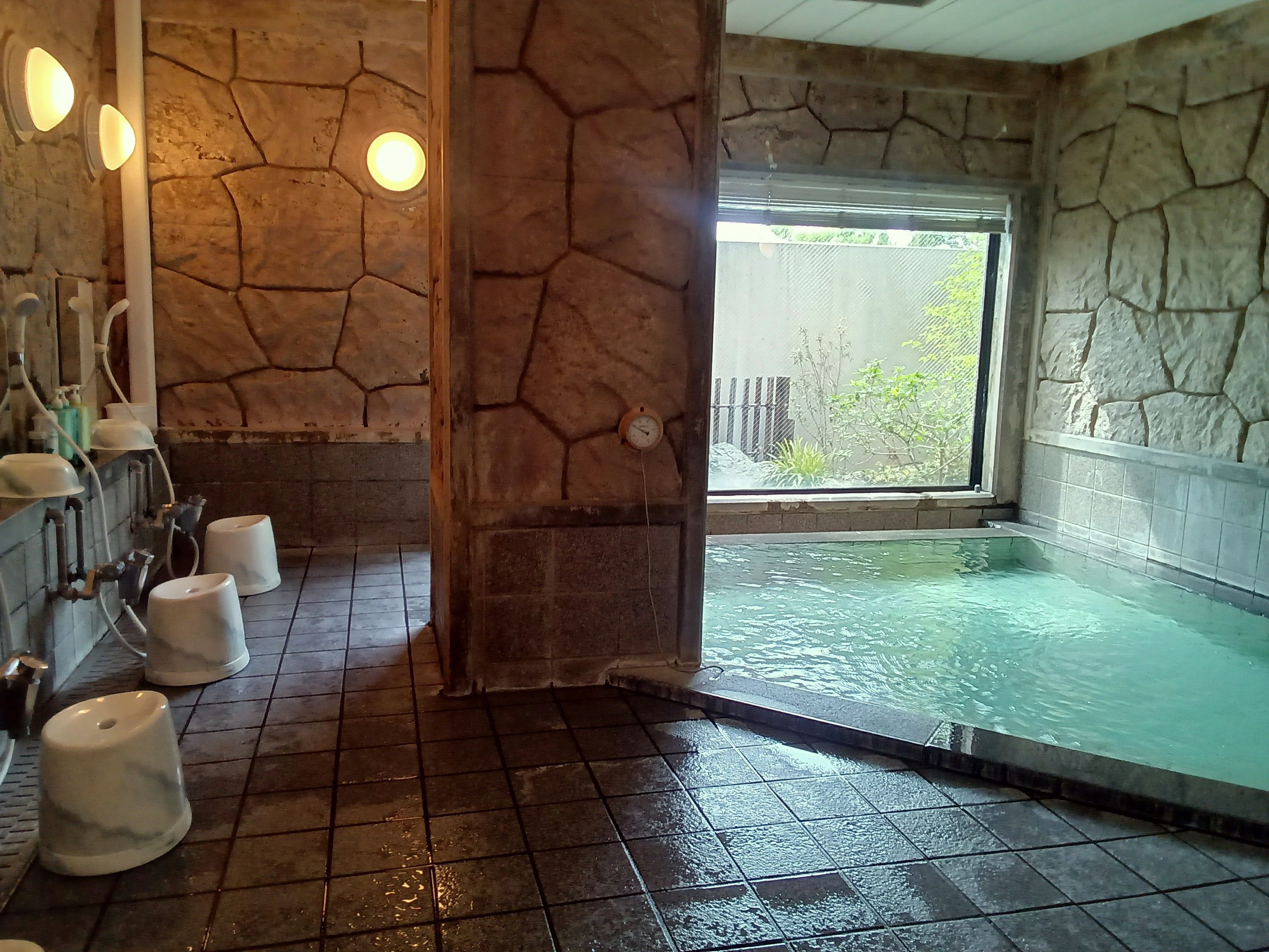 Un baño con pared de piedra, una ventana y una bañera.