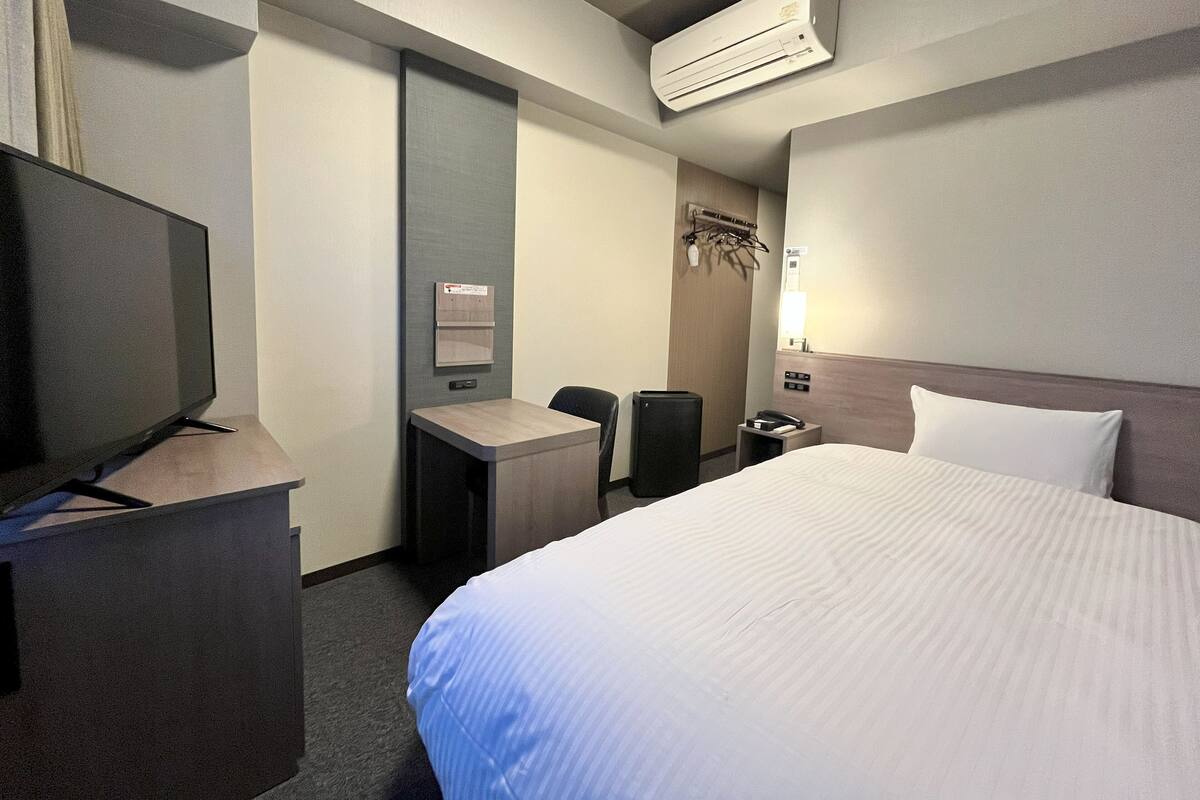 Ein Hotelzimmer mit Bett, Schreibtisch, Stuhl, Fernseher, Klimaanlage und Kleiderhaken.