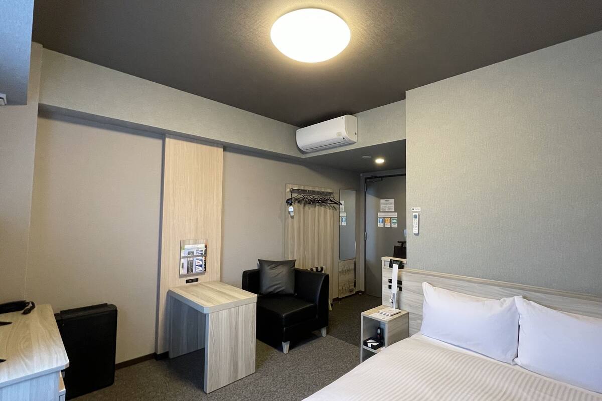 Ein Hotelzimmer mit einem Bett, einem Schreibtisch, einem Sessel, einem Fernseher und einer Klimaanlage.