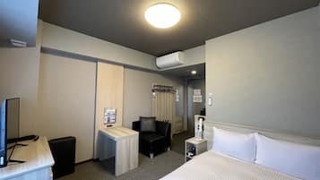 Una habitación de hotel con cama, escritorio, silla, televisor y aire acondicionado.