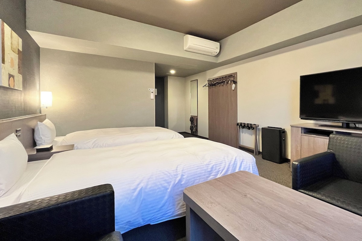 Ein Hotelzimmer mit zwei Betten, einem Fernseher, einem Schreibtisch und einem Stuhl.