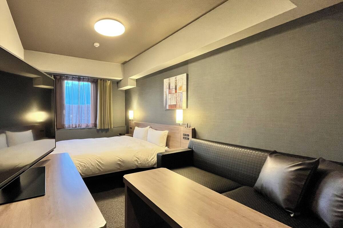 Ein Hotelzimmer mit Bett, Sofa, Tisch und einem fenster mit Vorhängen.
