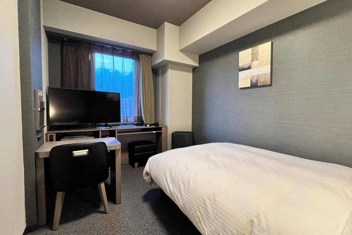Ein Hotelzimmer mit einem Bett, einem Schreibtisch mit Computer, einem Fernseher und einem Fenster mit Vorhängen.