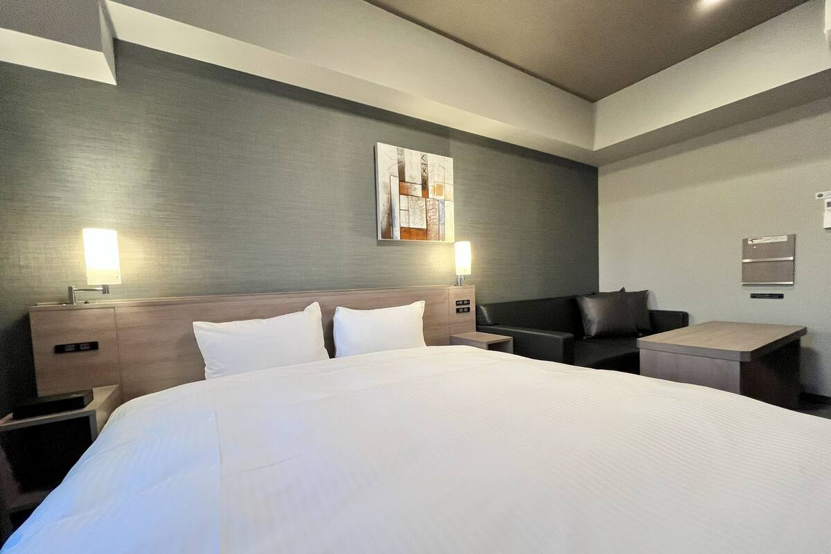 Ein Hotelzimmer mit einem großen Bett, einem Schreibtisch, einem Sessel und einer Couch. Es gibt zwei Nachttische mit Lampen.