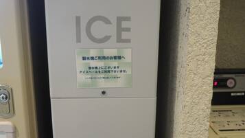 An ice dispenser with instructions in Japanese, located in a room with a textured wall and a control panel in the background.