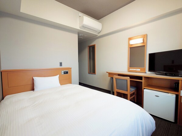 Une chambre d’hôtel comprenant un lit, un bureau avec une télévision et un petit réfrigérateur.