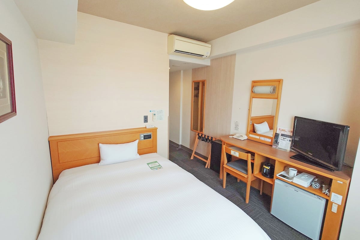 A hotel room with a bed, a desk with a computer, a TV, and a mini-fridge.