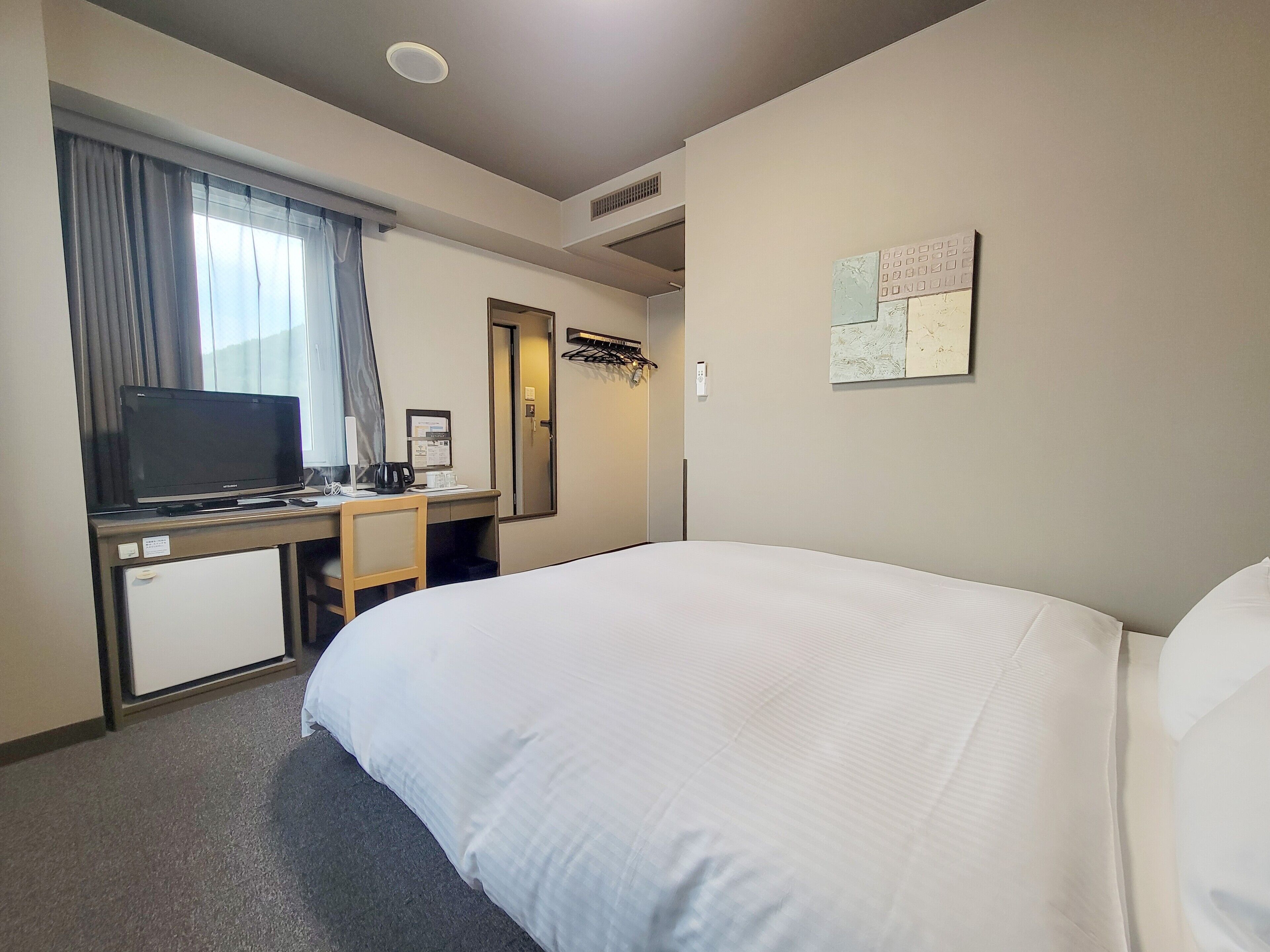 Habitación de hotel con cama, escritorio con televisor, refrigerador pequeño y puerta que da a un baño.