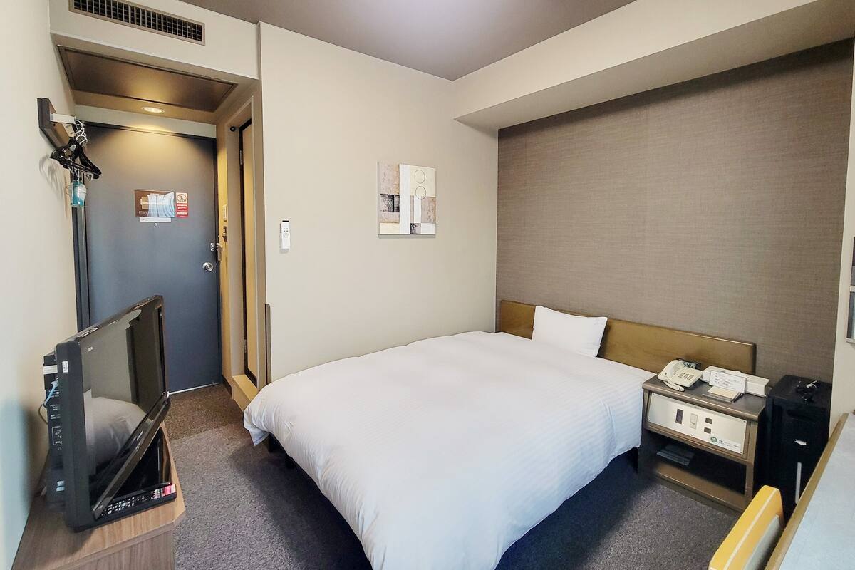 A hotel room with a bed, bedside table, and a television on a stand.