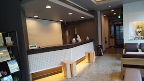 A hotel reception area with a tiled wall, a reception desk, and seating arrangements.