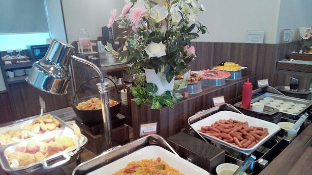 A buffet with various food items, including pasta, hot dogs, and pastries, along with a decorative flower arrangement.