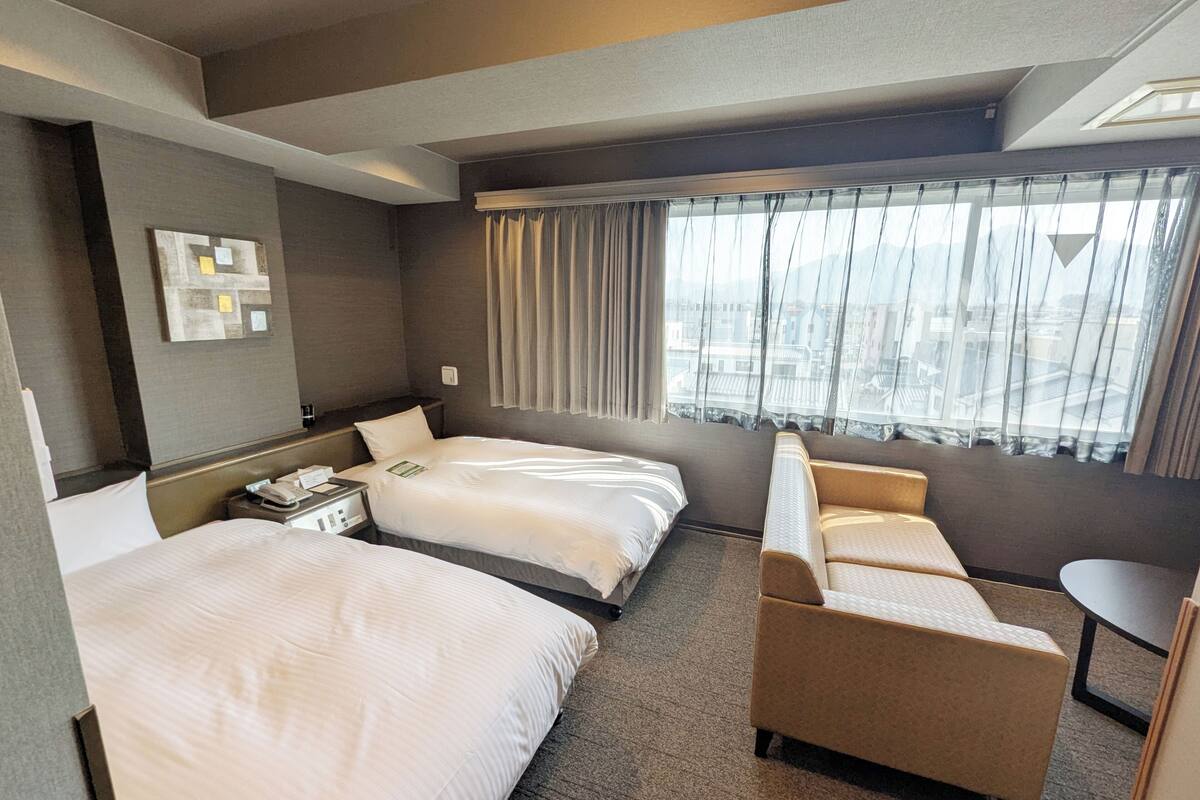 A hotel room with two beds, a sofa, a small table, and a window with curtains.