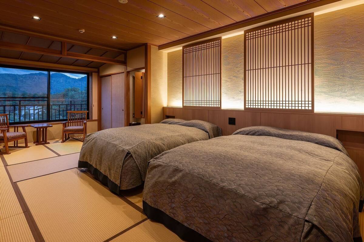 A traditional Japanese-style room with tatami flooring, two beds, a view of mountains, and sliding doors.