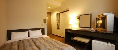 Habitación de hotel con cama, escritorio, refrigerador pequeño, lámpara y televisión.