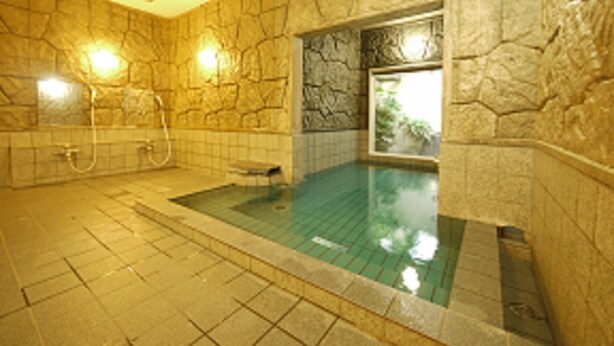 A stone-walled bathroom with a built-in hot tub, a shower area, and a window with a view of greenery.