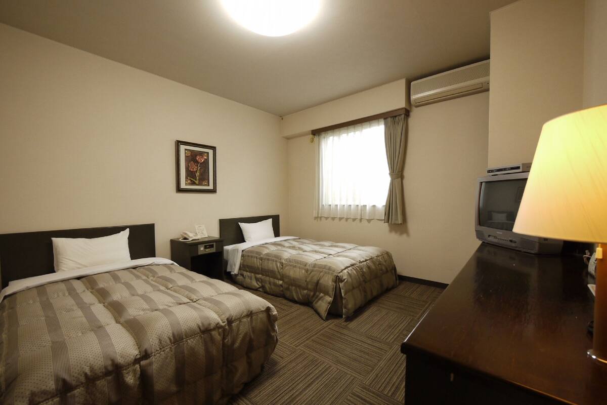 A hotel room with two beds, a desk, a television, and a painting on the wall.