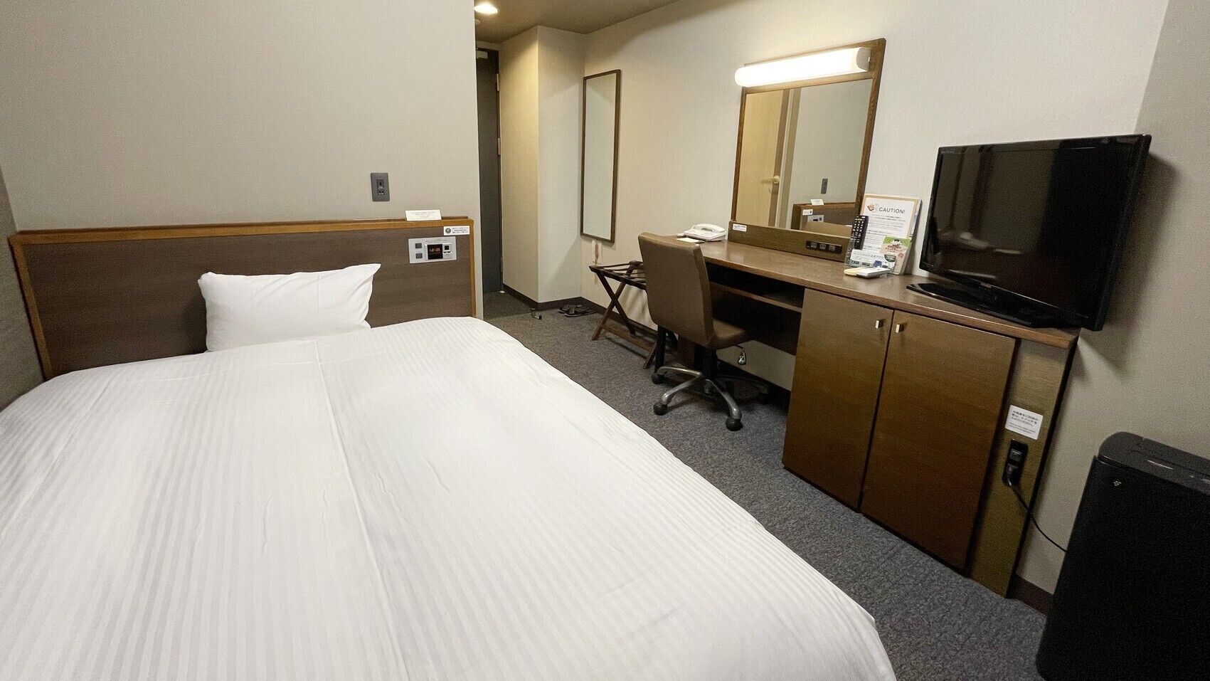 A hotel room with a bed, a desk, a chair, a television, and a mirror.