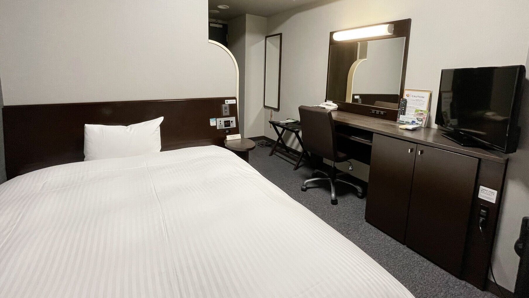 A hotel room with a bed, a desk, a chair, a television, and a mirror.