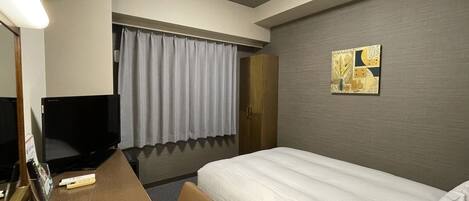 Une chambre d’hôtel avec un lit, un bureau avec une télévision, une chaise, un rideau et un tableau au mur.