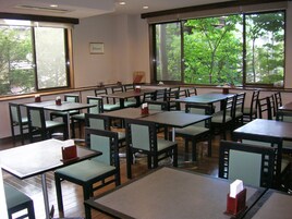 A restaurant with multiple tables and chairs, large windows with a view of trees, and a framed picture on the wall.