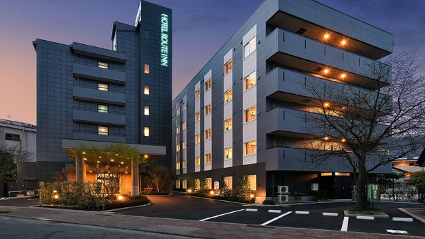 Un hôtel moderne, reconnaissable à son grand panneau « HOTEL ROUTEM », qui compte plusieurs étages et dont l’entrée est bien éclairée.