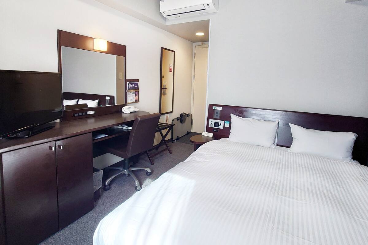 A hotel room with a bed, a desk with a computer, a TV, and a mirror.