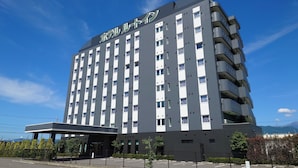 A multi-story hotel with a modern design, featuring a prominent entrance and a parking area in front. - Hotel Route Inn Komagane Inter (Komagane)