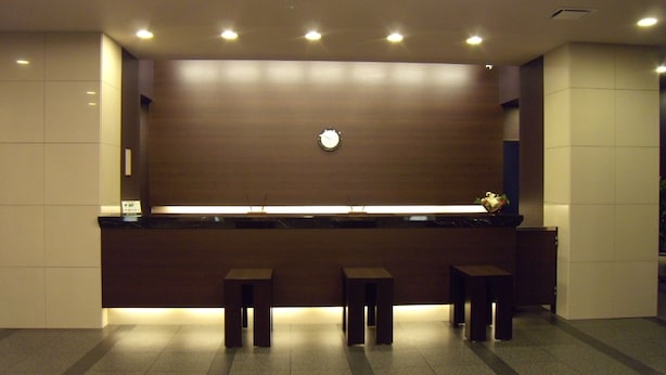 A modern reception area with a flat-screen TV, a clock, and three stools. - Hotel Route Inn Komagane Inter (Komagane)
