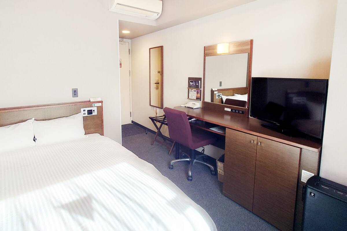 A hotel room with a large bed, a desk with a chair, a television, and a mirror.