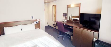 A hotel room with a large bed, a desk with a chair, a television, and a mirror.