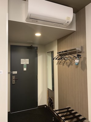 A hallway with a black door, an air conditioning unit mounted on the wall, and a coat rack with a spray bottle. - Hotel Route-Inn Komoro (Komoro)