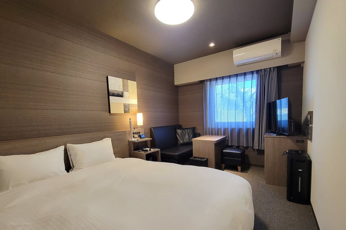 Quarto de hotel com uma cama grande, uma escrivaninha com cadeira, televisão e ar condicionado.