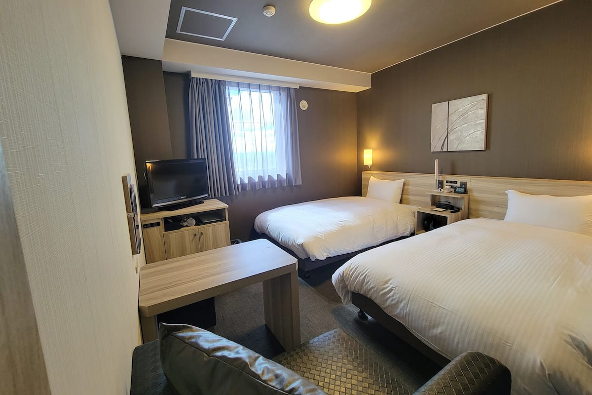 Quarto de hotel com duas camas, televisão, escrivaninha e uma pequena área de estar.