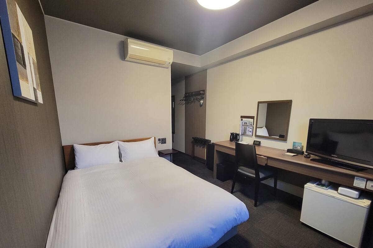 Quarto de hotel com cama, escrivaninha, televisão e frigorífico.