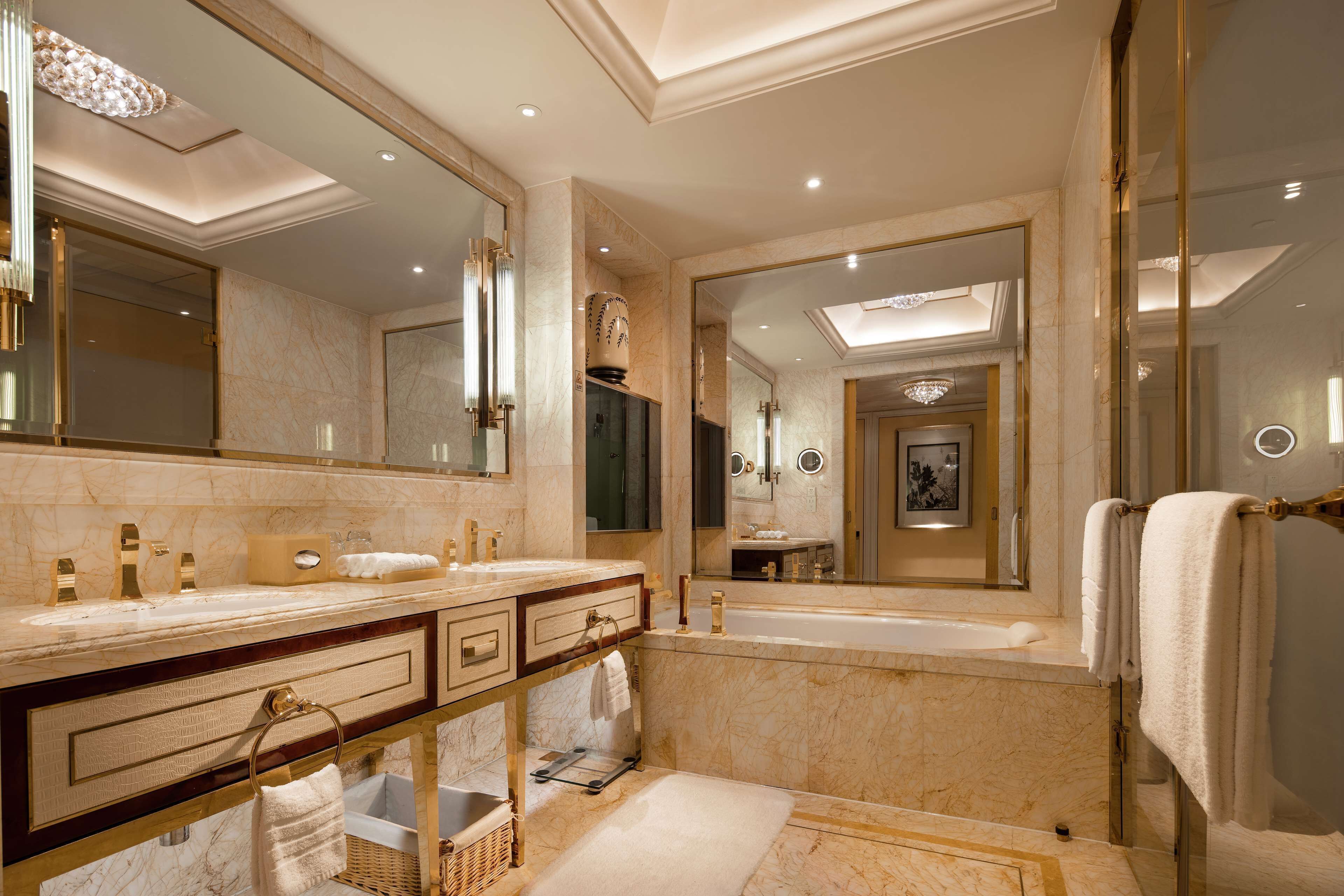 A luxurious bathroom with marble countertops, dual sinks, a large mirror, and a bathtub.