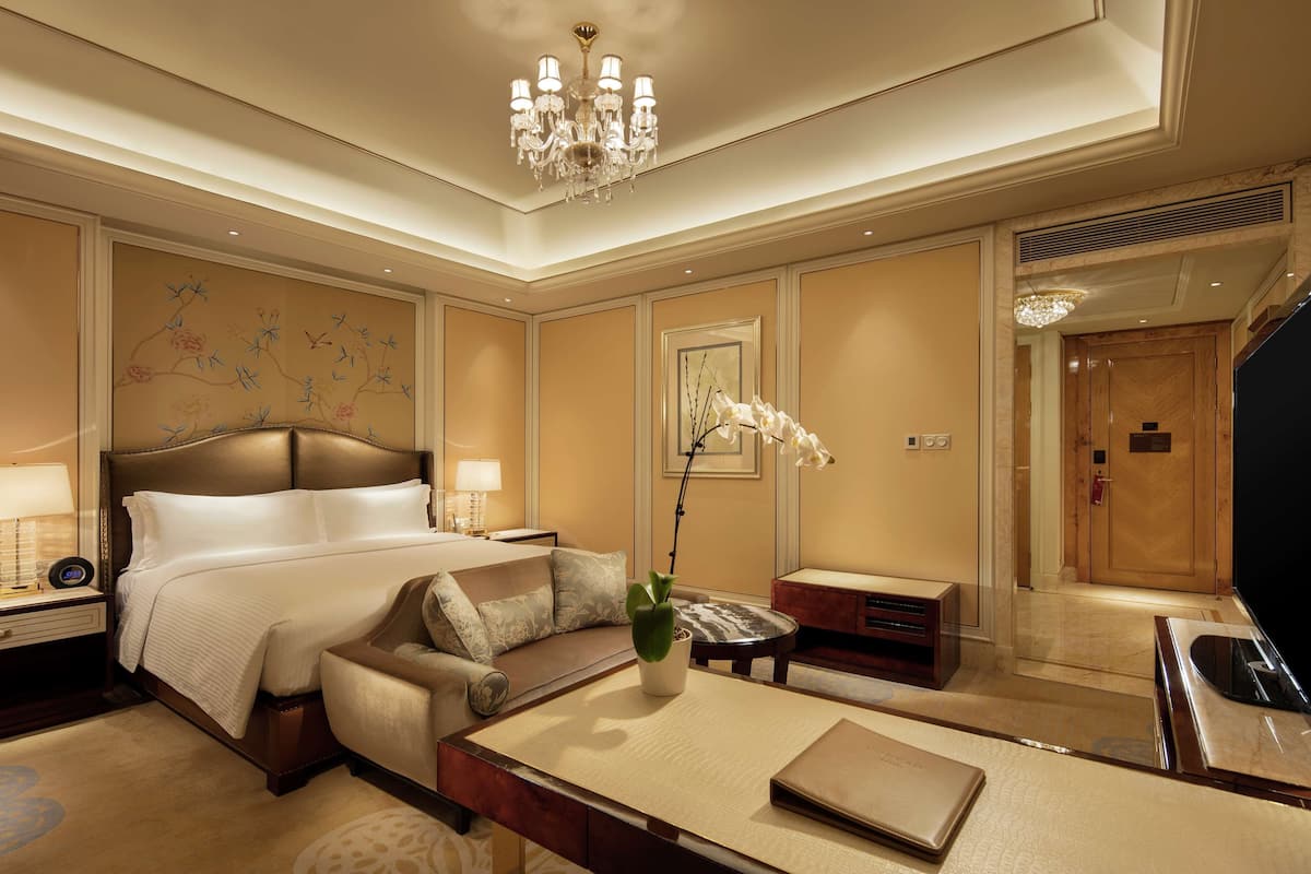 Ein Hotelzimmer mit einem großen Bett, einem Sofa, einem Couchtisch, einem Fernseher und einer Chandelüster.