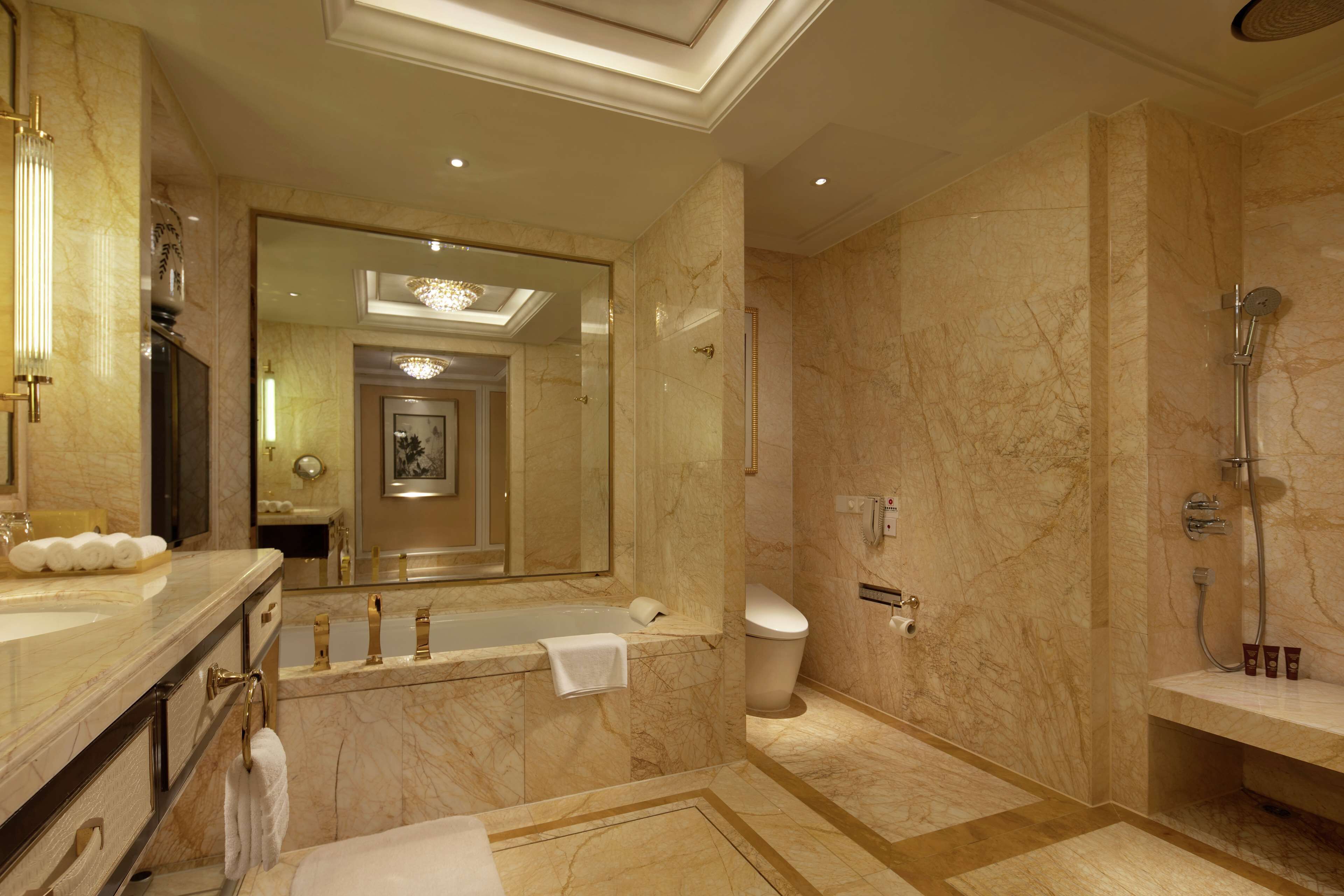 A luxurious bathroom with a marble floor, a large mirror, a bathtub, a toilet, and a shower area.