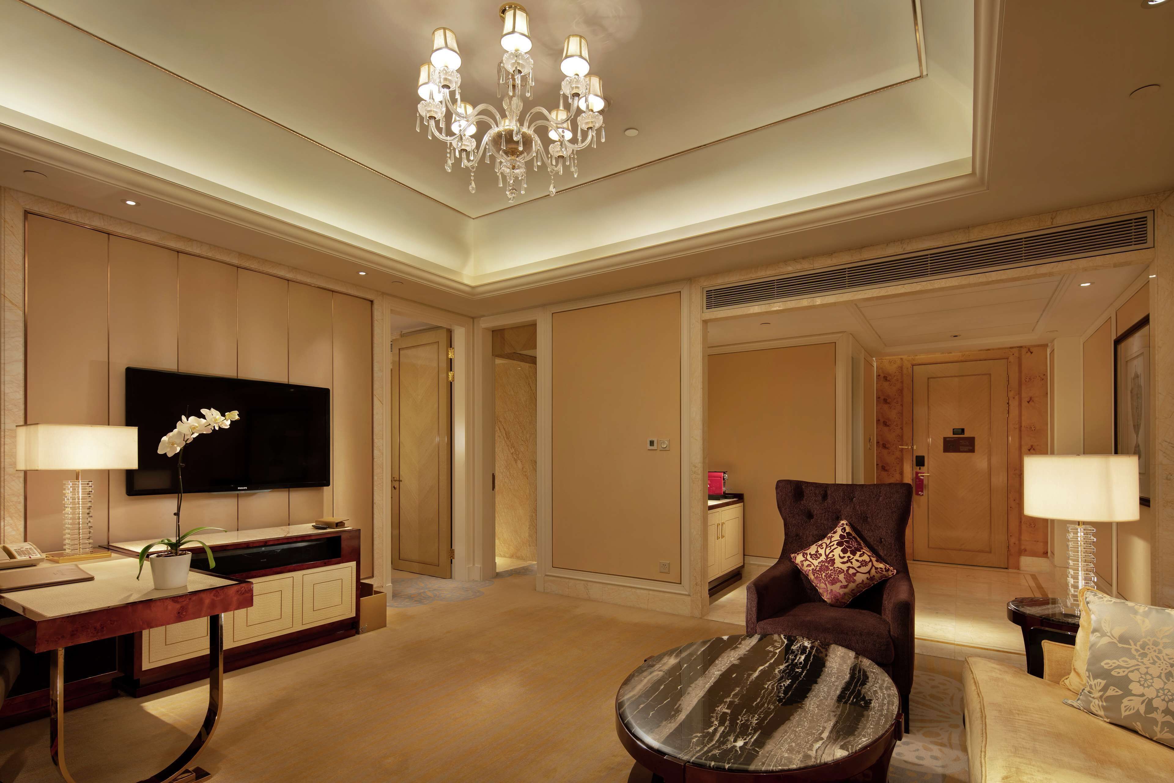 A spacious living room with a flat-screen TV, a chandelier, a potted orchid, and a comfortable seating area.