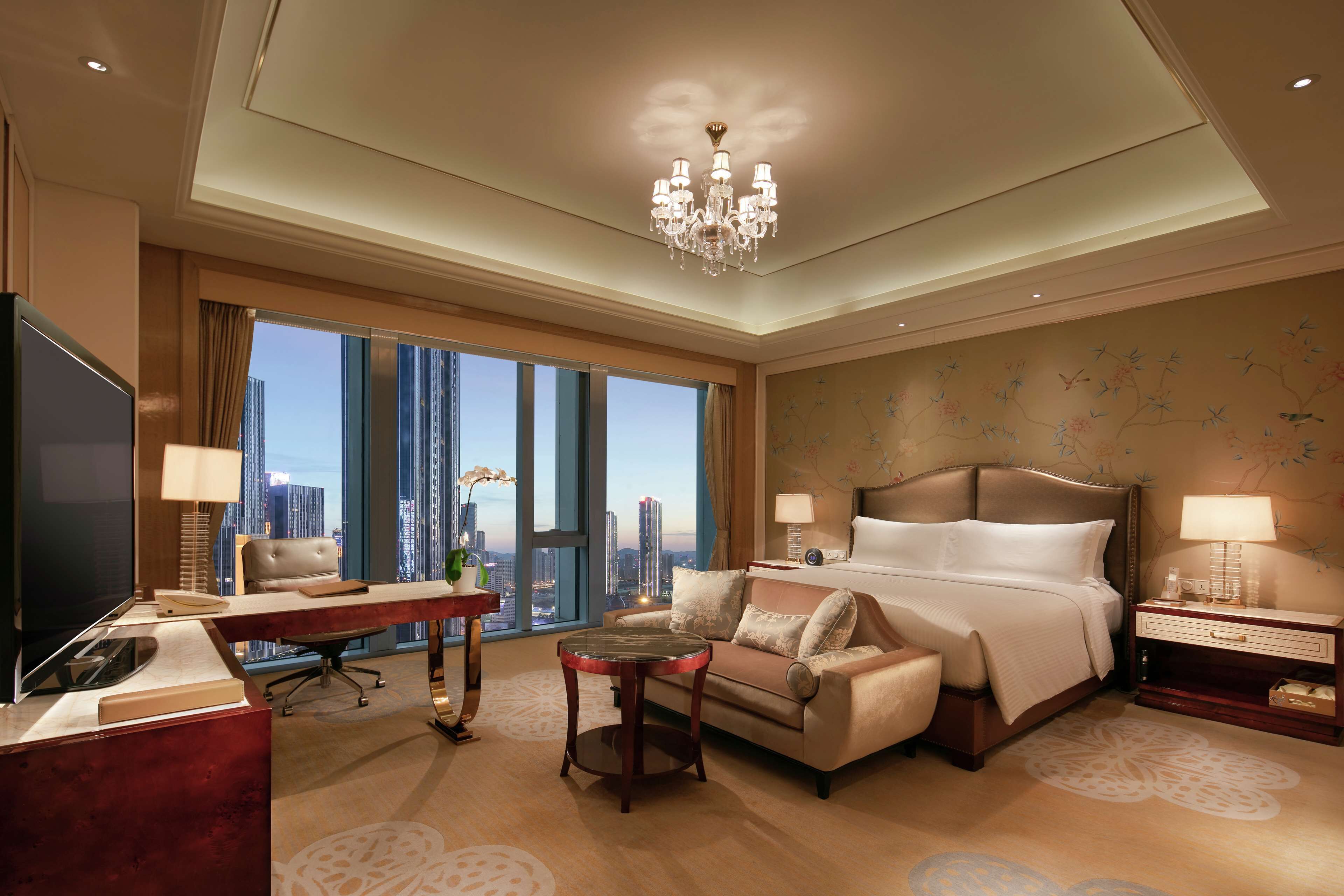 Une chambre d’hôtel avec un grand lit, un bureau avec un ordinateur, une télévision et une vue sur la ville.